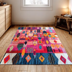 May include: A colourful rectangular rug with a patchwork design. The rug features geometric shapes in pink, red, blue, orange, and yellow. The rug is placed on a wooden floor in a room with natural light. The rug measures approximately 200cm x 300cm.