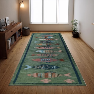May include: A rectangular green rug with a dark blue border. The rug features a repeating pattern of colourful fish in shades of pink, blue, orange, and yellow. The rug is placed on a hardwood floor.