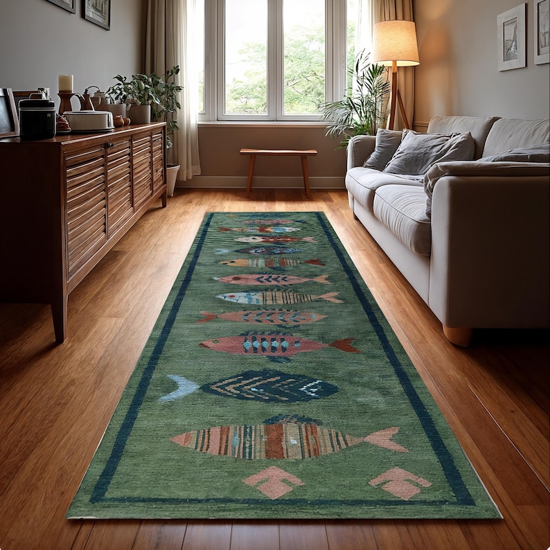 May include: A green rectangular rug with a dark blue border and a repeating pattern of colourful fish. The fish designs include shades of red, blue, orange, and pink. The rug is placed on a hardwood floor in a living room setting.
