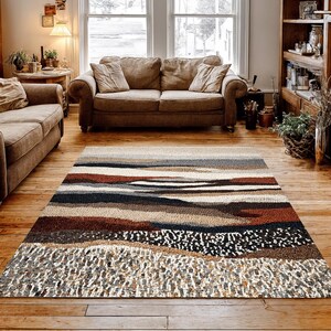 May include: A rectangular area rug with a landscape design. The rug features horizontal bands of color, including shades of brown, gray, and white. The rug is placed on a hardwood floor in a living room setting.