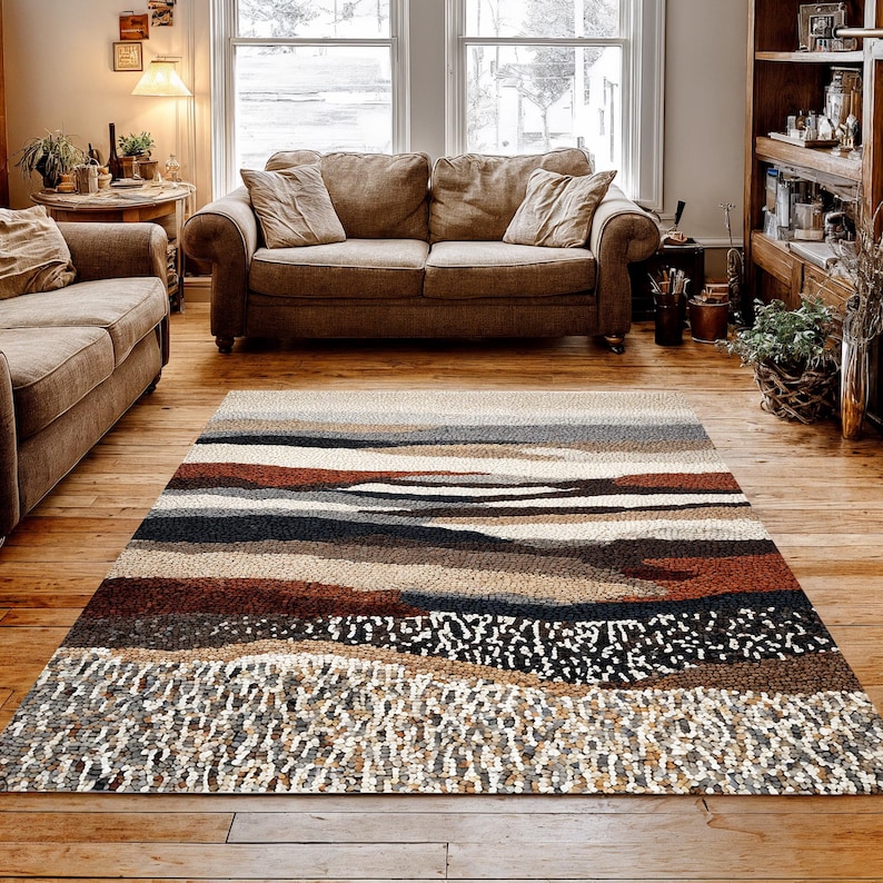 May include: A rectangular area rug with a landscape design. The rug features horizontal bands of color, including shades of brown, gray, and white. The rug is placed on a hardwood floor in a living room setting.