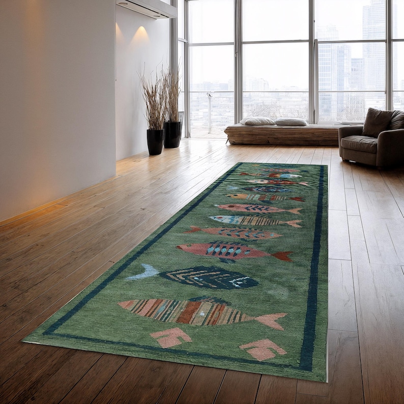 May include: A rectangular green rug with a dark blue border. The rug features a repeating pattern of colourful fish in shades of pink, blue, orange, and yellow. The rug is placed on a hardwood floor.
