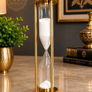 Peut inclure: Un grand sablier doté d'une structure en métal doré poli avec des supports cylindriques et des plaques circulaires en haut et en bas. Le récipient en verre transparent contient du sable blanc fin qui s'écoule de la chambre supérieure vers l'inférieure.