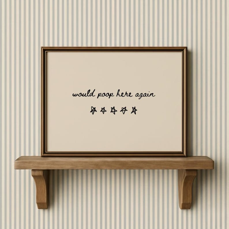 May include: A framed print with the text "would poop here again" and five star symbols. The frame is brown, and the print is displayed on a wooden shelf. The background features a striped wallpaper.