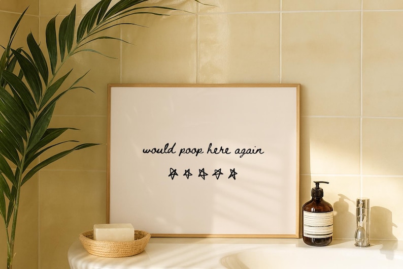 May include: A framed print with the text "would poop here again" and five star symbols. A brown soap dispenser, a small hourglass, and a woven basket with a bar of soap are also visible.
