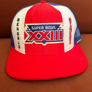 Puede incluir: Gorra de camionero roja, blanca y azul del Super Bowl XXII, con los logotipos de los Bengals y los 49ers. La gorra tiene una visera roja, una corona roja, blanca y azul y una parte trasera de malla azul. El texto "Super Bowl XXII" es visible.