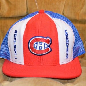 Puede incluir: Una gorra de béisbol roja, blanca y azul con un logotipo de los Montreal Canadiens. La gorra tiene una parte trasera de malla y las palabras "Montreal Canadiens" están bordadas en los lados.
