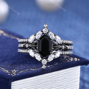 May include: A black and white engagement ring set featuring a central black gemstone in an octagonal shape, surrounded by smaller white gemstones. The set includes a matching band and two additional bands, all with intricate detailing.