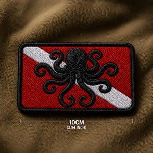 Op de afbeelding: Geborduurde rechthoekige patch met een rode achtergrond, witte diagonale streep en een zwart octopusontwerp. De patch meet 10 cm (3,94 inch) lang en heeft een zwarte rand. De patch is geborduurd.