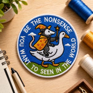 May include: A circular embroidered patch featuring a wizard opossum riding a white goose. The opossum wears a yellow star-patterned hat and cloak, holding a star wand. The blue background includes the text BE THE NONSENSE YOU WANT TO SEE IN THE WORLD.