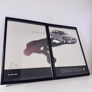 May include: Two framed prints. One features a silver BMW car with the text "MORE PUNCH THAN EVER." The other print shows the car and BMW branding. The text "The New 328i" is at the bottom of one print. The prints are in black frames.