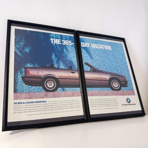 Könnte beinhalten: Zwei gerahmte Vintage-Werbeanzeigen für BMW-Cabrios. Die Poster zeigen ein lila Cabrio mit dem Text "THE 365-DAY VACATION" und "THE NEW ALL-SEASON CONVERTIBLE" vor blauem Hintergrund. Die Rahmen sind schwarz.