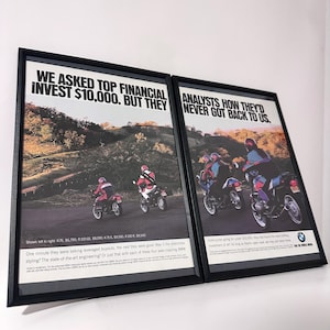 以下が含まれることがあります： 曲がりくねった道を走るライダーを描いた、BMWのバイク広告の額入りポスター2枚。テキストには「WE ASKED TOP FINANCIAL ANALYSTS HOW THEY'D INVEST $10,000. BUT THEY NEVER GOT BACK TO US.」と書かれています。ポスターにはバイクの画像とBMWのロゴが含まれています。