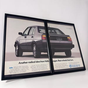 Puede incluir: Dos impresiones enmarcadas que presentan un Volkswagen Jetta plateado. Las impresiones muestran un anuncio con el texto "Another radical idea from Volks" y "Rear wheels that turn." El coche se muestra de perfil y trasero.