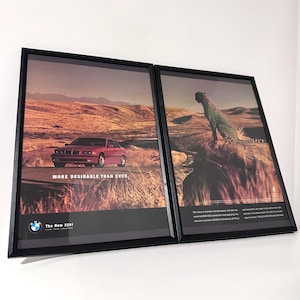 Könnte beinhalten: Zwei gerahmte BMW-Werbeanzeigen. Eine zeigt ein rotes Auto auf einer Wüstenstraße mit dem Text "MORE DESIRABLE THAN EVER". Die andere zeigt einen Geparden auf einem Felsen. Beide sind in schwarzen Rahmen.