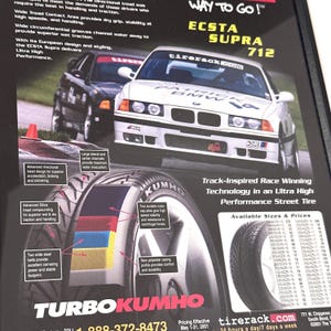 Könnte beinhalten: Werbung für Kumho-Reifen mit einem weißen BMW-Rennwagen und dem Text "ECSTA SUPRA 712". Die Anzeige hebt Reifeneigenschaften mit Diagrammen und Text hervor, darunter "Track-Inspired Race Winning Technology".