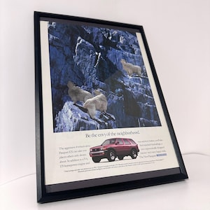 May include: Framed advertisement featuring a maroon SUV on a rocky mountain backdrop with three white goats. Text reads "Be the envy of the neighborhood." and details about the vehicle.