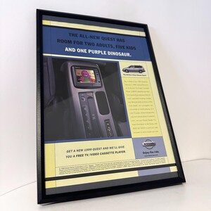 May include: A framed vintage 1999 Nissan Quest advertisement featuring a blue and yellow color scheme. The text reads: THE ALL-NEW QUEST HAS ROOM FOR TWO ADULTS, FIVE KIDS AND ONE PURPLE DINOSAUR. It includes an image of a car interior with a TV screen.