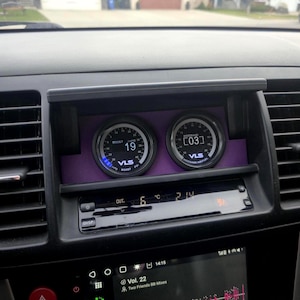Könnte beinhalten: Autoinstrumententafel mit zwei runden Messgeräten, die Messwerte anzeigen. Das linke Messgerät zeigt "BOOST 19" mit blauem Licht, das rechte "WIDEBAND AIRFUEL [03]" an. Die Messgeräte sind in einer lila Platte in einem schwarzen Armaturenbrett.