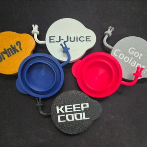 Puede incluir: Una colección de tapones de botella coloridos y de forma única. Cada tapón tiene un color y texto diferente, incluyendo "Drink?", "EJ-JUICE", "Got Coolant?" y "KEEP COOL". Los tapones tienen un diseño caprichoso con brazos y manos.