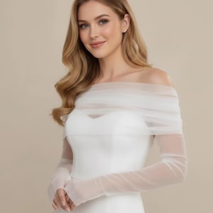 Könnte beinhalten: Ein weißes schulterfreies Brautkleid mit langen, durchsichtigen Ärmeln. Das Kleid hat einen herzförmigen Ausschnitt und ein figurbetontes Oberteil. Die Ärmel sind aus zartem, fließendem Stoff gefertigt.