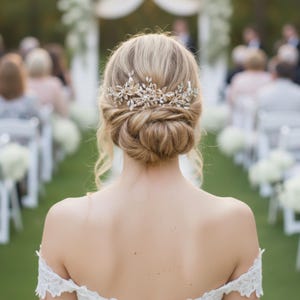 Könnte beinhalten: Eine Braut in einem weißen schulterfreien Brautkleid aus Spitze, mit einem tiefen Dutt und einem dekorativen Haarschmuck. Die Zeremonie findet im Freien statt, mit Gästen, die auf beiden Seiten eines grünen Rasens sitzen.