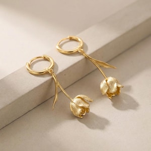 Op de afbeelding: Een paar goudkleurige tulpenoorbellen. Elke oorbel heeft een creoolsluiting en een delicate steel met een blad, die uitmondt in een getextureerde tulpbloem. De oorbellen worden op een neutraal oppervlak gepresenteerd.