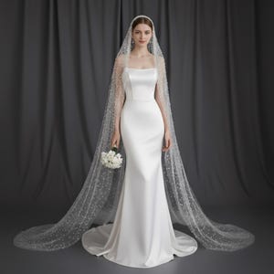 May include: A white satin wedding dress with a square neckline and a mermaid silhouette. The bride wears a pearl-studded veil and holds a bouquet of white flowers. The background is a dark gray curtain.