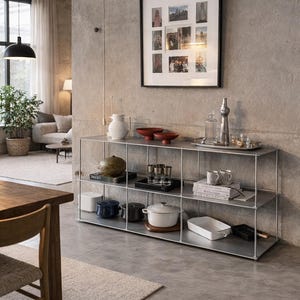 May include: A contemporary living space with a metal shelving unit displaying kitchenware and decorative objects. A framed photo collage is mounted on the wall above. The room has a neutral colour scheme, with a concrete wall and grey flooring.