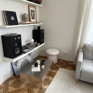 May include: A modern living room with a stainless steel coffee table, a white rug, and a gray sofa. Shelves display art, vinyl records, and speakers. The room has a minimalist aesthetic with a neutral color palette.