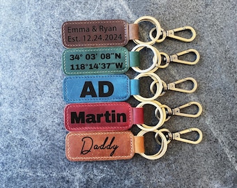 May include: A collection of personalized leather keychains in various colors, each with a metal ring and clasp. The keychains are engraved with names, initials, and dates. The colors include brown, green, blue, red, and tan.