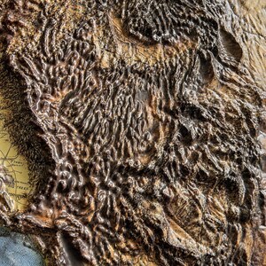 May include: A detailed relief map of a mountainous region, likely the western United States. The map features textured, raised areas in shades of brown and tan, with visible geographical features. The map has a vintage aesthetic, with some text visible.