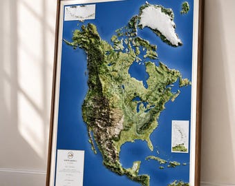 May include: A framed 3D relief map of North America, showcasing the continent's topography with detailed green and brown landmasses against a blue ocean background. The map is encased in a dark wooden frame with a white border, leaning against a wall.
