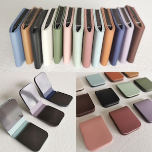 May include: A collection of rectangular magnetic clips in various solid colors including blue, tan, black, white, green, pink, and purple. The clips feature a smooth, matte-textured exterior and a dark interior surface with a strong magnetic closure.