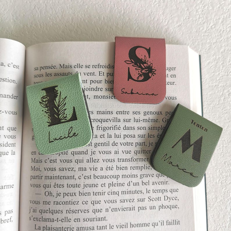 Trois marque-pages en simili cuir personnalisés avec initiales et prénoms gravés, en vert clair, rose et vert foncé