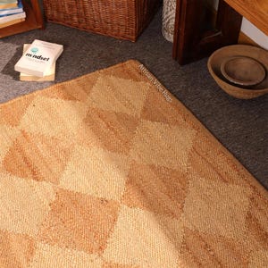 May include: A geometric patterned rug in shades of tan and beige. The rug has a diamond pattern and is made of a woven material. The text "Artisan Vibe Rugs" is visible on the rug's edge. The word "mindset" is visible on a book.