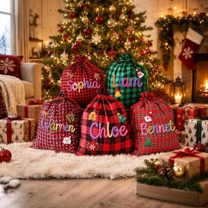 Puede incluir: Cinco bolsas de regalo de tela con cordón, con patrones de cuadros rojos y negros o verdes y negros. Cada bolsa está personalizada con un nombre bordado de colores: Sophia, Liam, Warren, Chloe y Bennet, y decorada con pequeños apliques de fieltro navideños.