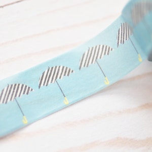 May include: A roll of blue washi tape with a repeating pattern of black and white striped umbrellas with yellow handles.