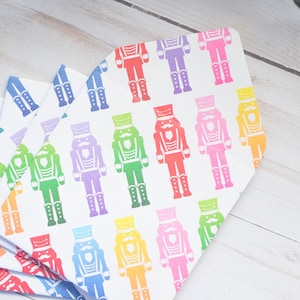 May include: A stack of white paper envelopes featuring a repeating pattern of colourful nutcracker soldier illustrations. The nutcrackers are in various colours, including red, pink, yellow, green, blue, and purple.