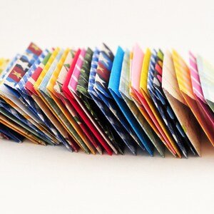 May include: A stack of colorful folded paper envelopes with various patterns, including polka dots, stripes, and floral designs.
