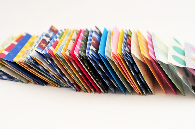 May include: A stack of colorful folded paper envelopes with various patterns, including polka dots, stripes, and floral designs.