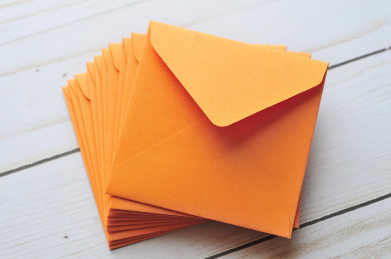 Pode incluir: Uma pilha de envelopes laranja, com o envelope superior dobrado ao meio para criar uma aba pontiaguda.