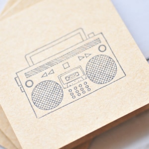 May include: A stack of brown note cards with a black and white line drawing of a vintage boombox on the top card.