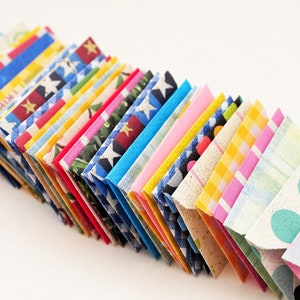 May include: A stack of colorful folded paper envelopes with various patterns, including stars, polka dots, stripes, and plaid.