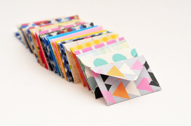 May include: A stack of colorful patterned envelopes with geometric designs. The top envelope has a light blue, pink, and orange geometric pattern.