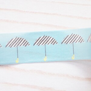 May include: A roll of blue washi tape with a repeating pattern of black and white striped umbrellas with yellow handles.