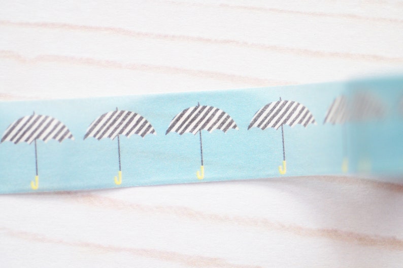 May include: A roll of blue washi tape with a repeating pattern of black and white striped umbrellas with yellow handles.
