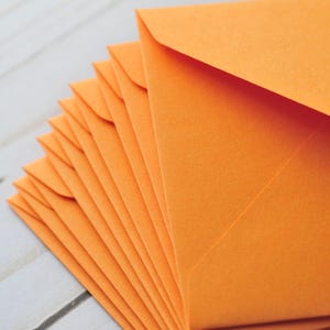 Pode incluir: Uma pilha de envelopes laranja, dobrados e prontos para serem usados para enviar cartas ou cart&otilde;es.