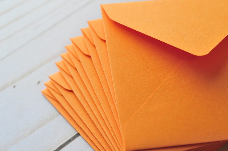 Pode incluir: Uma pilha de envelopes laranja, dobrados e prontos para serem usados para enviar cartas ou cart&otilde;es.