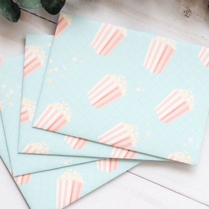 May include: Four light blue envelopes with a pink and white popcorn pattern. The envelopes are stacked on top of each other.
